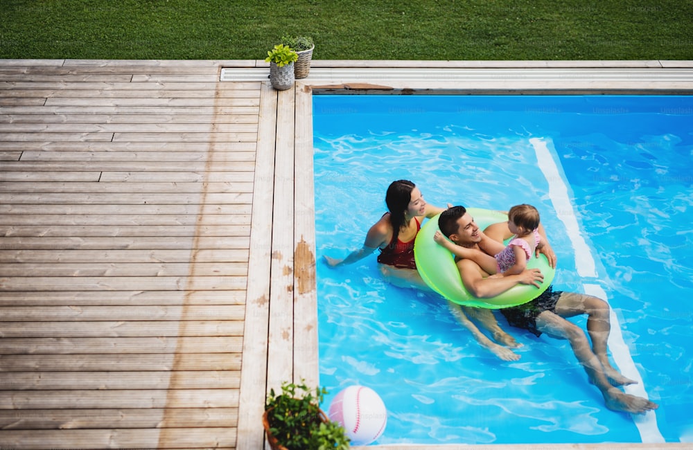 Vista superior de la familia joven con hija pequeña en la piscina al aire libre en el jardín del patio trasero.
