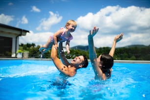 Happy young family with small daughter in swimming pool outdoors in backyard garden, playing.