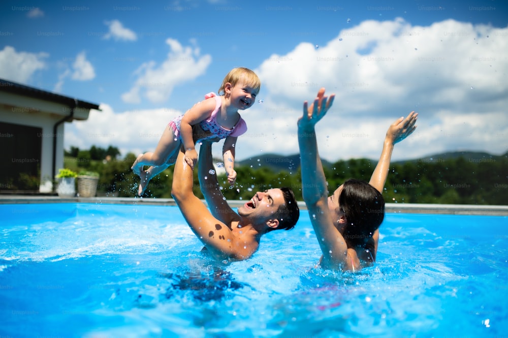 Giovane famiglia felice con la piccola figlia in piscina all'aperto nel giardino del cortile, giocando.