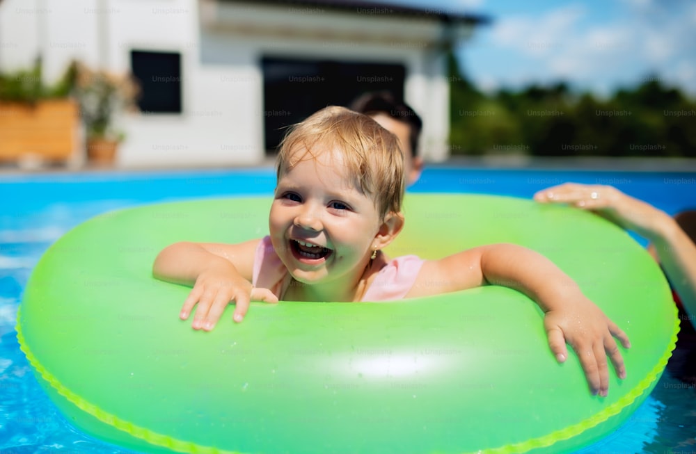 Happy young family with small daughter in swimming pool outdoors in backyard garden.