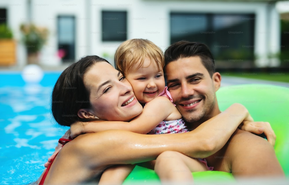 Jeune famille heureuse avec petite fille dans la piscine extérieure dans le jardin arrière.