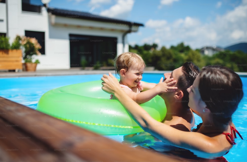 Familia joven feliz con hija pequeña en piscina al aire libre en el jardín del patio trasero.