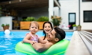 뒤뜰 정원에 있는 야외 수영장에서 작은 딸과 함께 행복한 젊은 가족.