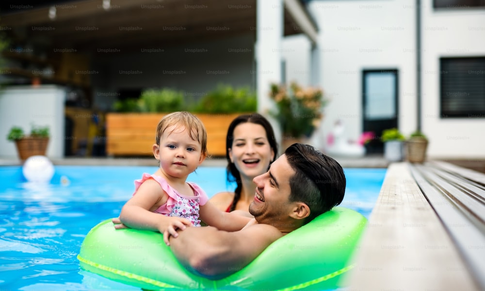 Happy young family with small daughter in swimming pool outdoors in backyard garden.