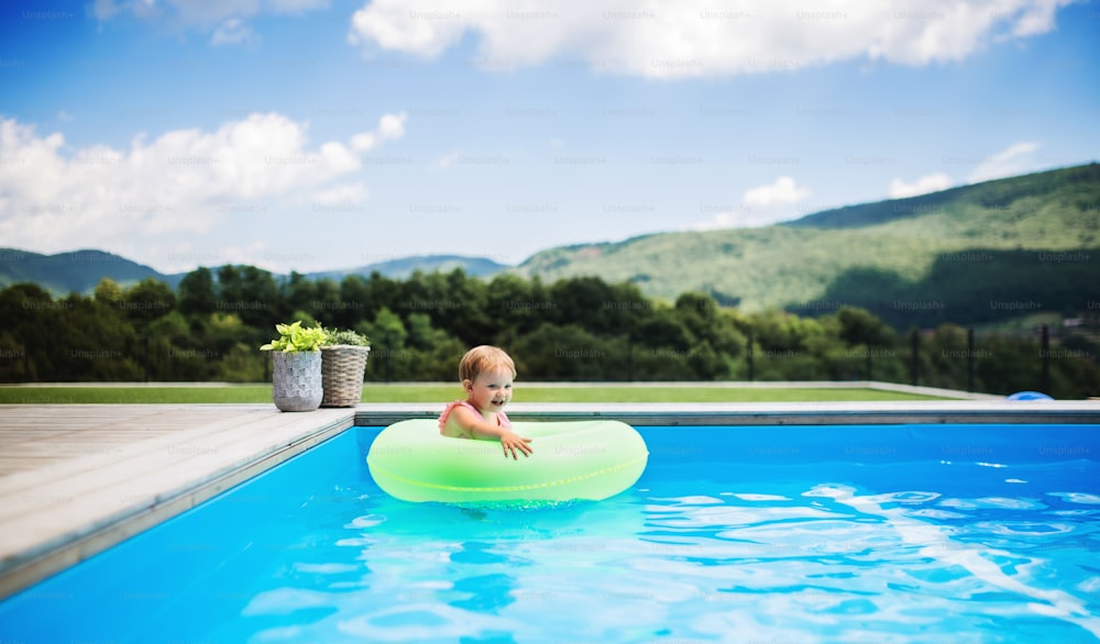 Portrait of small toddler girl with inflatable ring in swimming pool outdoors in backyard garden.
