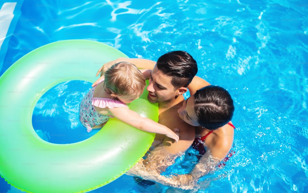 뒤뜰 정원에 있는 야외 수영장에서 작은 딸과 함께 있는 젊은 가족의 최고 전망.
