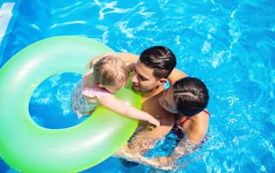 Top view of young family with small daughter in swimming pool outdoors in backyard garden.