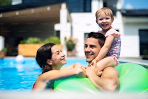 Giovane famiglia felice con la piccola figlia in piscina all'aperto nel giardino del cortile.