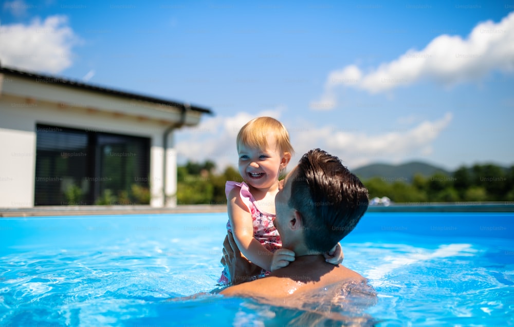 Young father with small daughter in swimming pool outdoors in backyard garden, playing.