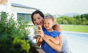 Ritratto di giovane madre con la piccola figlia all'aperto nel giardino del cortile, spruzzando piante.