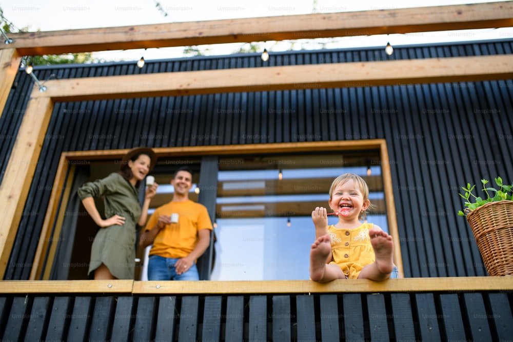 Vista de bajo ángulo de una familia joven con una hija pequeña al aire libre, fin de semana en una casa de contenedores en el campo.