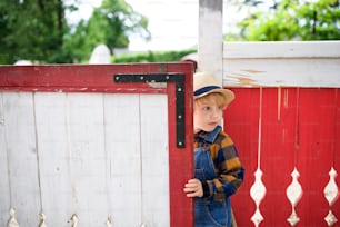 Ritratto di ragazzino nella fattoria, apertura cancello rosso e bianco.