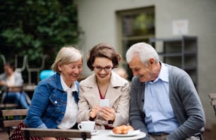 Portrait of woman with senior parents sitting outdoors in cafe, using smartphone.