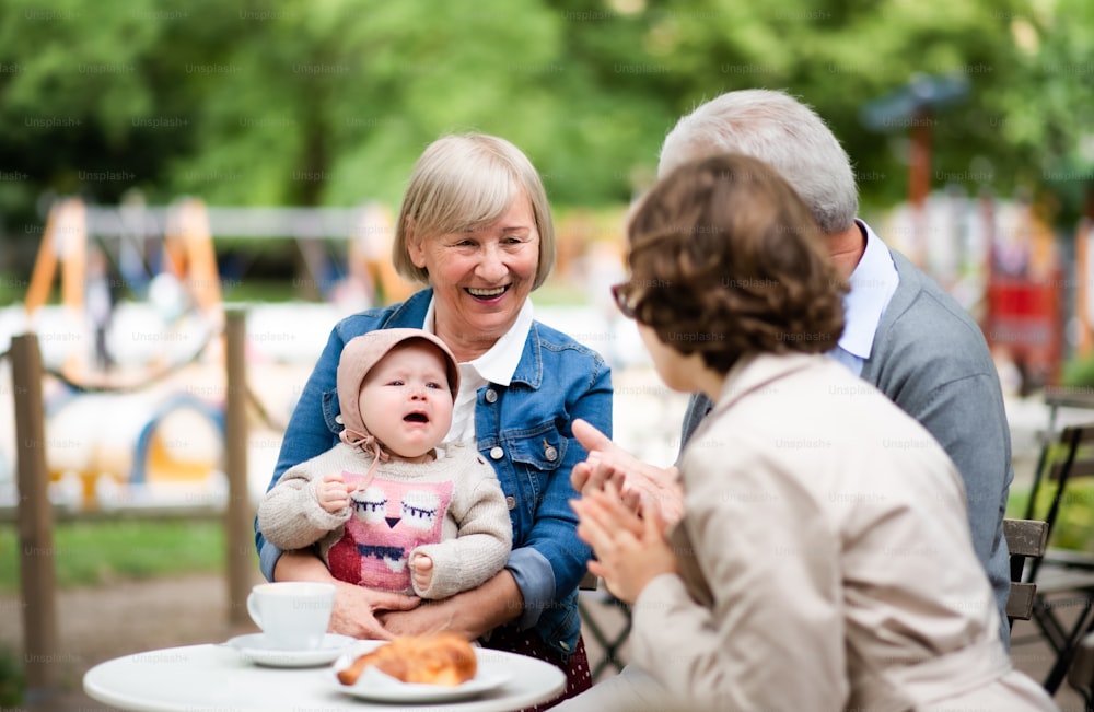 Happy senior couple with daughter and baby granddaughter sitting outdoors in cafe, talking.