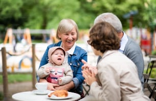 Happy senior couple with daughter and baby granddaughter sitting outdoors in cafe, talking.