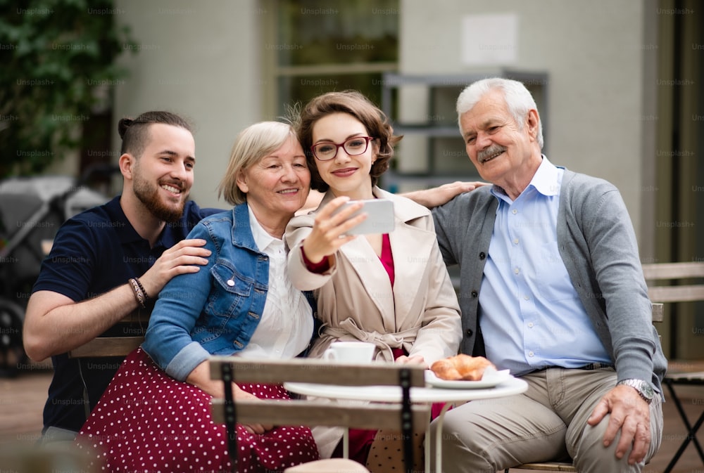 Happy senior couple with adult son and daughter sitting outdoors in cafe, taking selfie.