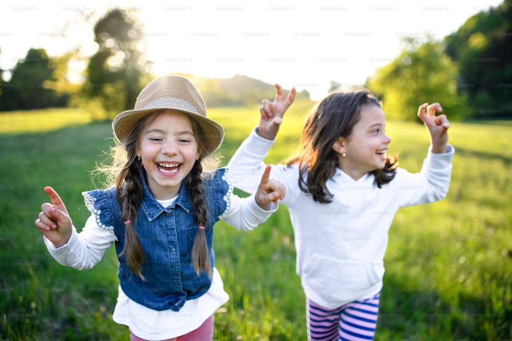 Front view portrait of two small girls standing outdoors in spring nature, laughing.