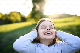 Retrato en primer plano de una niña pequeña parada al aire libre en la naturaleza primaveral, divirtiéndose.