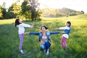 Front view of mother with two small daughters having fun outdoors in spring nature, pulling hair.