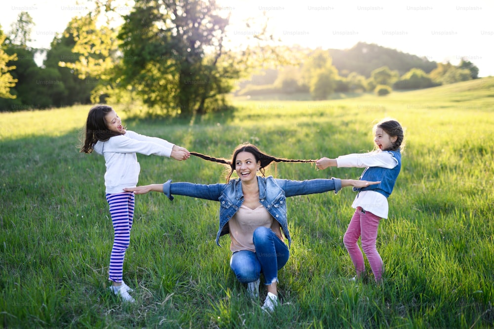 Vista frontal de la madre con dos hijas pequeñas divirtiéndose al aire libre en la naturaleza primaveral, tirando del pelo.