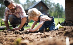 Padre maduro con hijo pequeño trabajando al aire libre en jardín, concepto de estilo de vida sostenible.