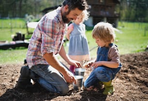 Reifer Vater mit kleinen Kindern, die draußen im Garten arbeiten, nachhaltiges Lifestyle-Konzept.