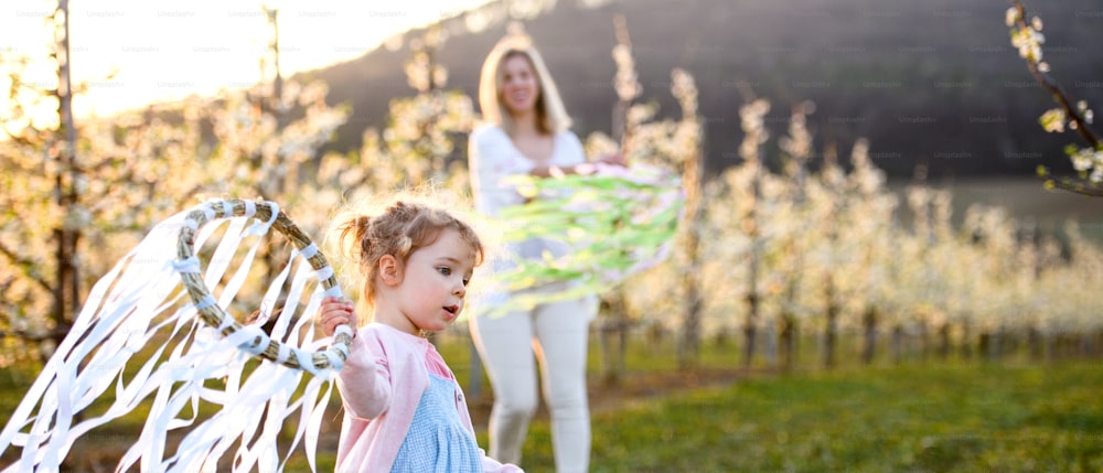 Small girl with unrecognizable mother playing outdoors in spring nature at sunset.