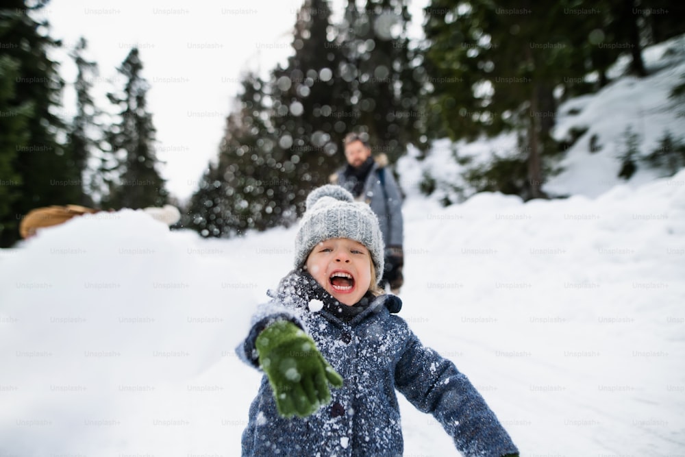 Front view of happy small child playing in snow, holiday in winter nature.