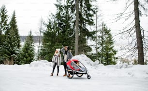 Father and mother with two small children sitting in trailer, walking in snow in winter nature.