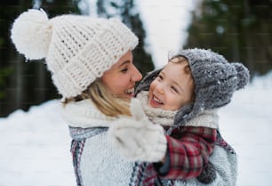 Vista lateral da mãe alegre com a filha pequena em pé na natureza do inverno, rindo.
