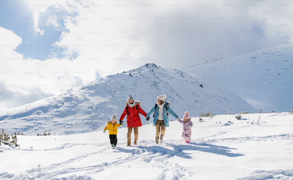 Retrato frontal de padre y madre con dos niños pequeños en la naturaleza invernal, caminando en la nieve.
