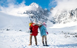 雪の中を歩く、冬の自然の中で2人の小さな子供を持つ父と母の背面図のポートレート。
