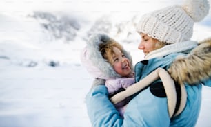 Ritratto di madre con la piccola figlia felice in piedi nella natura invernale, riposando.