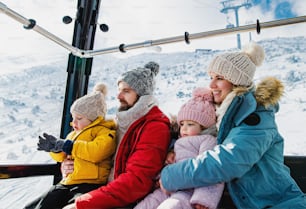 Familia feliz con un hijo pequeño y una hija dentro de una cabina de teleférico, vacaciones en la naturaleza nevada del invierno.