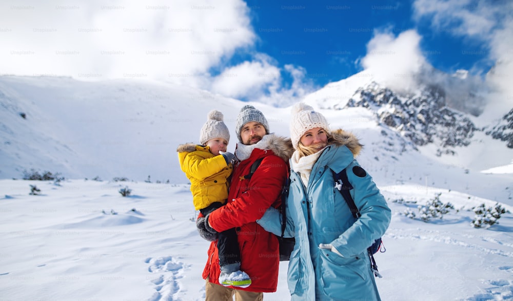 Retrato frontal de padre y madre con un hijo pequeño en la naturaleza invernal, de pie en la nieve.