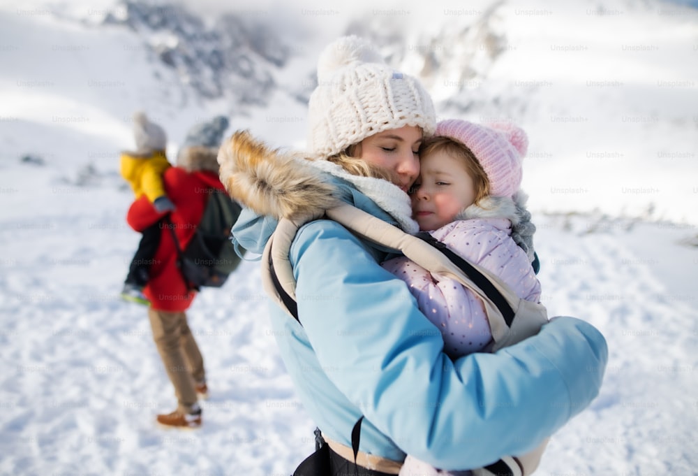 Portrait of mother with happy small daughter in carrier standing in winter nature, resting.
