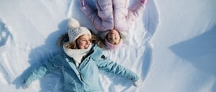 冬の自然の中で雪の中に横たわる小さな幼児の娘を持つ陽気な母親の上面図のポートレート。