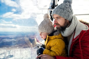 Padre con un hijo pequeño dentro de una cabina de teleférico, vacaciones en la naturaleza nevada del invierno. Espacio de copia.