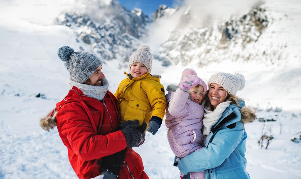 Portrait de face d’un père et d’une mère avec deux jeunes enfants dans la nature hivernale, debout dans la neige.
