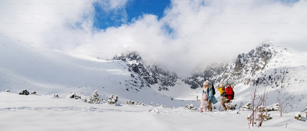 Portrait de face d’un père et d’une mère avec deux jeunes enfants dans la nature hivernale, jouant dans la neige.