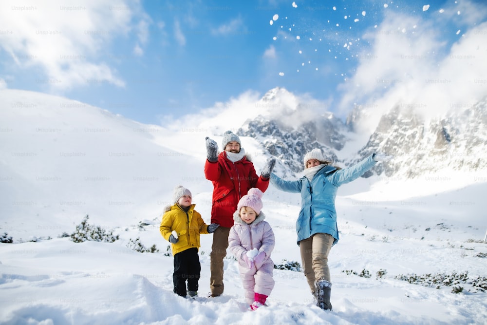 Portrait de face d’un père et d’une mère avec deux jeunes enfants dans la nature hivernale, jouant dans la neige.