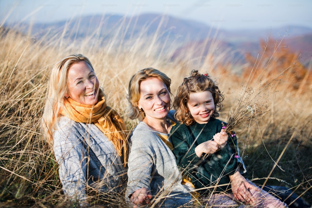 Portrait of small girl with mother and grandmother resting in autumn nature.