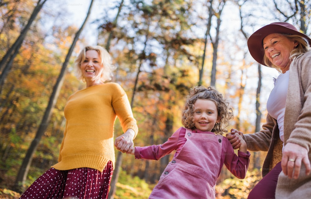 Small girl with mother and grandmother on a walk in autumn forest, having fun.