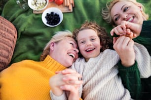 Top view of small girl with mother and grandmother having picnic in nature, laughing.