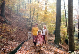 Small girl with mother and grandmother on a walk in autumn forest, talking.