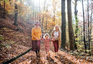 Small girl with mother and grandmother on a walk in autumn forest, running.