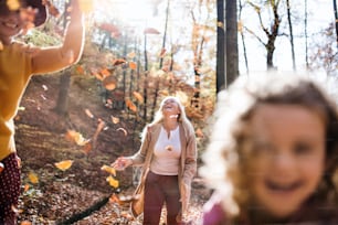 Happy small girl with mother and grandmother on a walk in autumn forest, midsection.