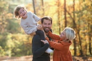 Beautiful young family with small daughter on a walk in autumn forest, having fun.