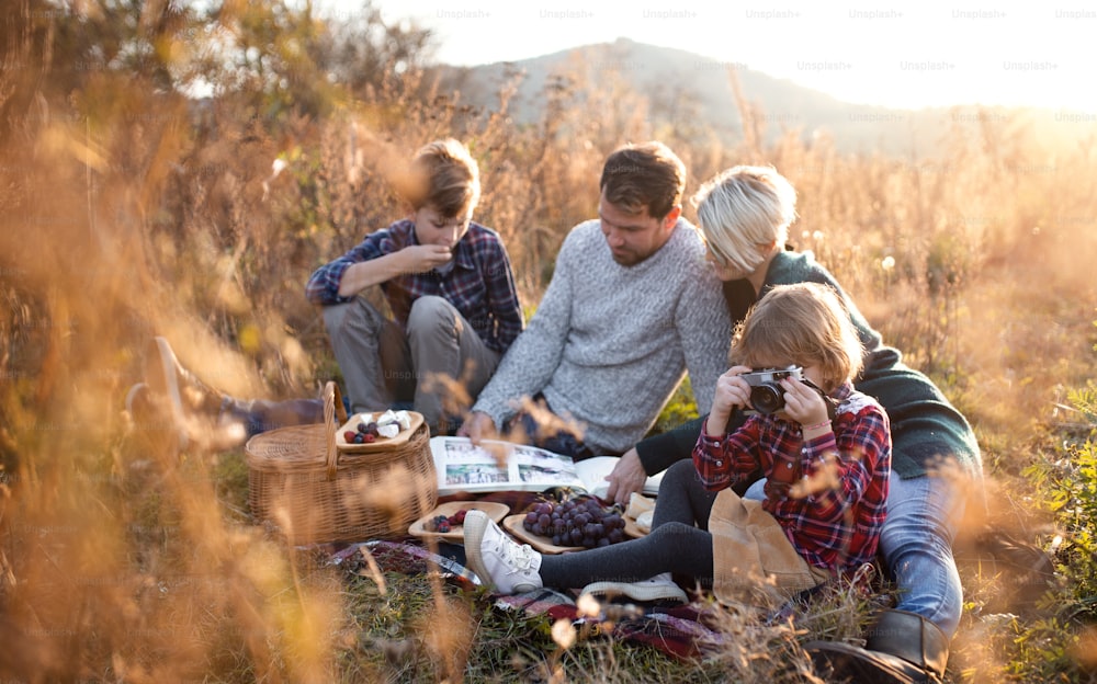 Beautiful young family with small children having picnic in autumn nature, sitting on grass.