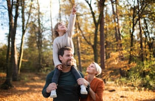 Beautiful young family with small daughter on a walk in autumn forest, having fun.